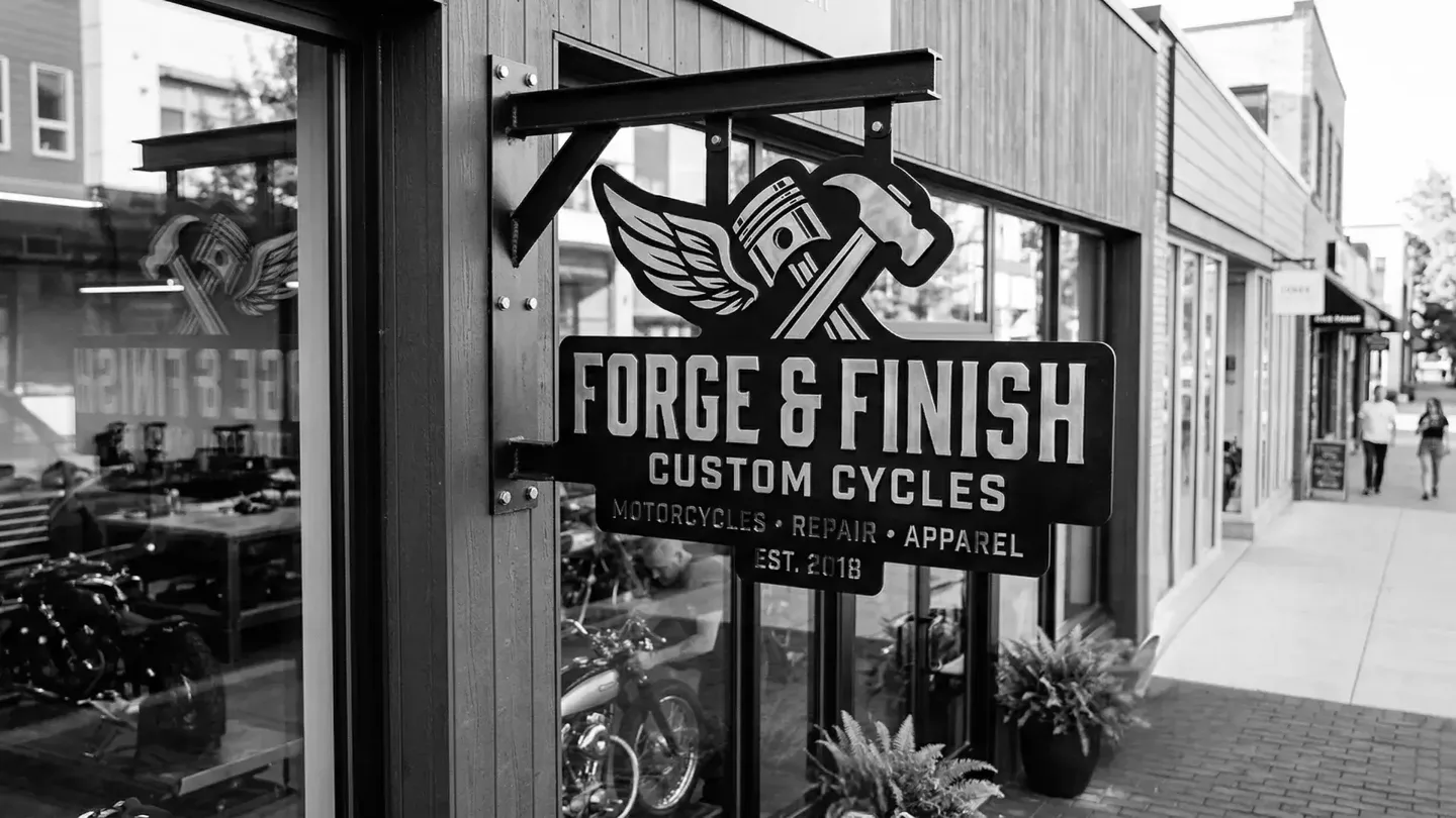 Custom signage displayed outside a storefront, featuring a hanging metal sign for a motorcycle shop